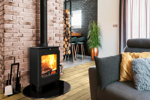 Portway Arundel 5kW Wood Burning Stove with flames on a black oval hearth against a brick wall