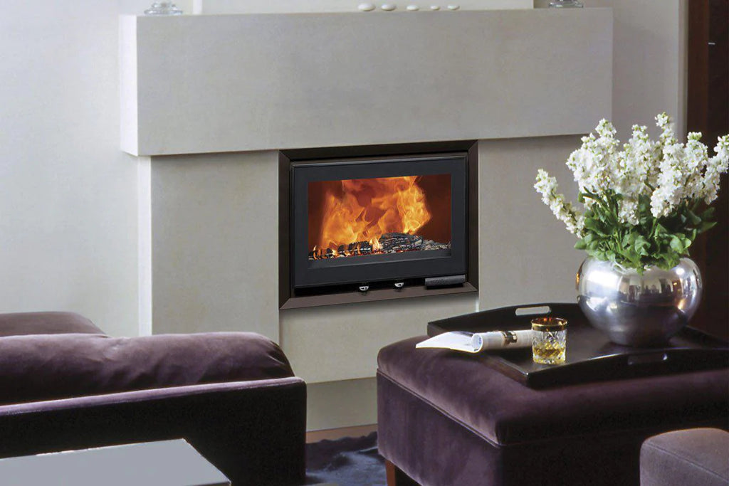 Fondis - V80L - 11.5kW Inset Wood Stove with flames in a lounging area with an armchair and an ottoman